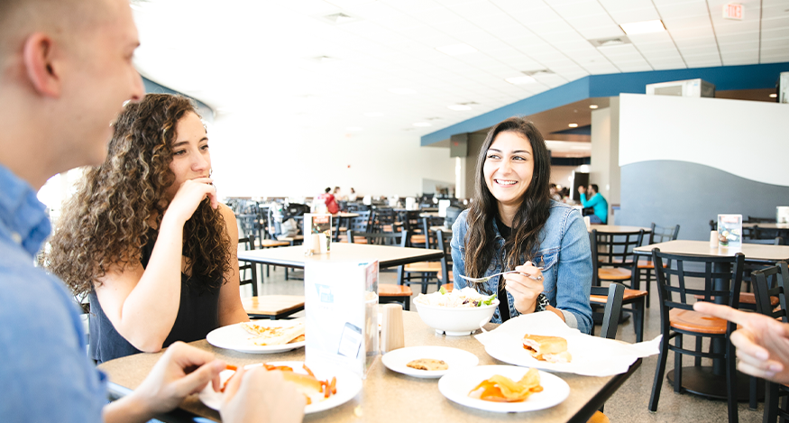 Three students sitting at a coffee shop drinking coffee and smiling